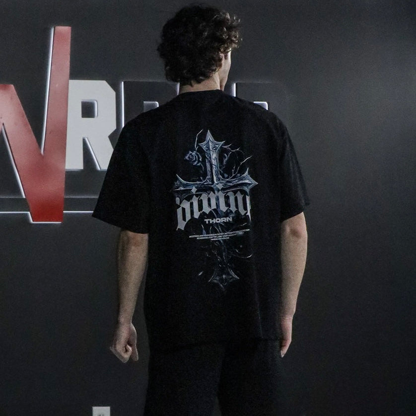 Person wearing a black t-shirt with a logo on the back, standing in front of a dark background with visible text.