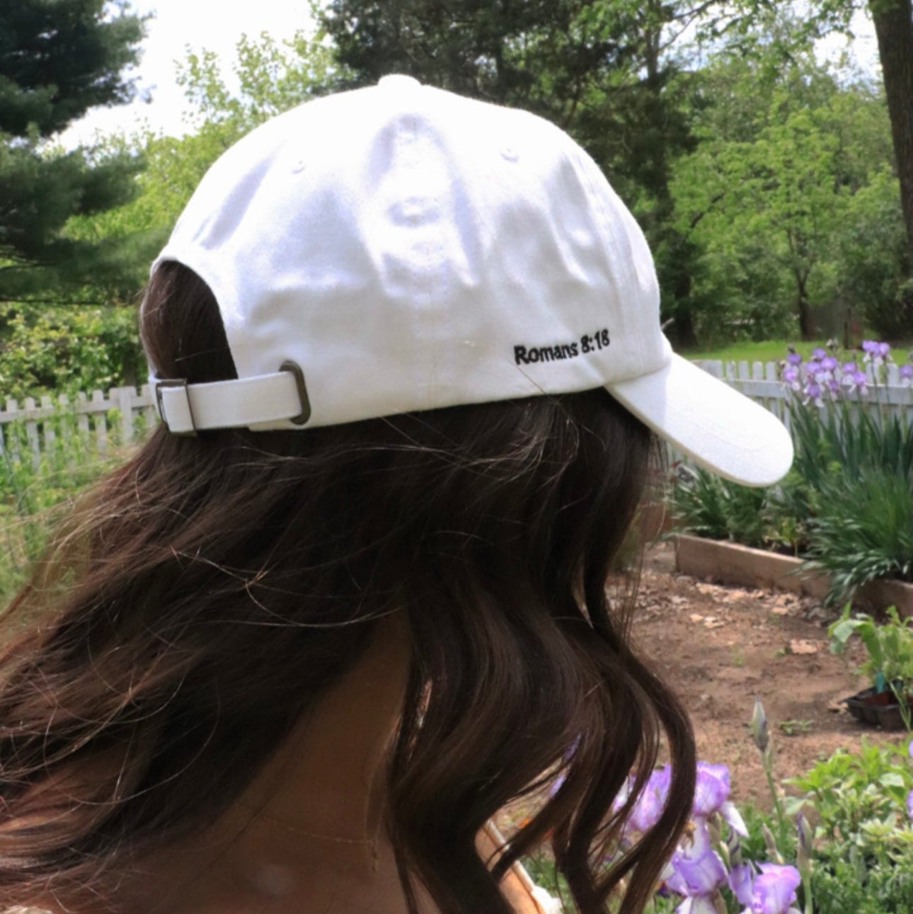 Person wearing a white cap with text in a garden setting